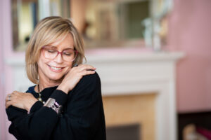 Woman in her mid fifties with glasses posing in her living room.